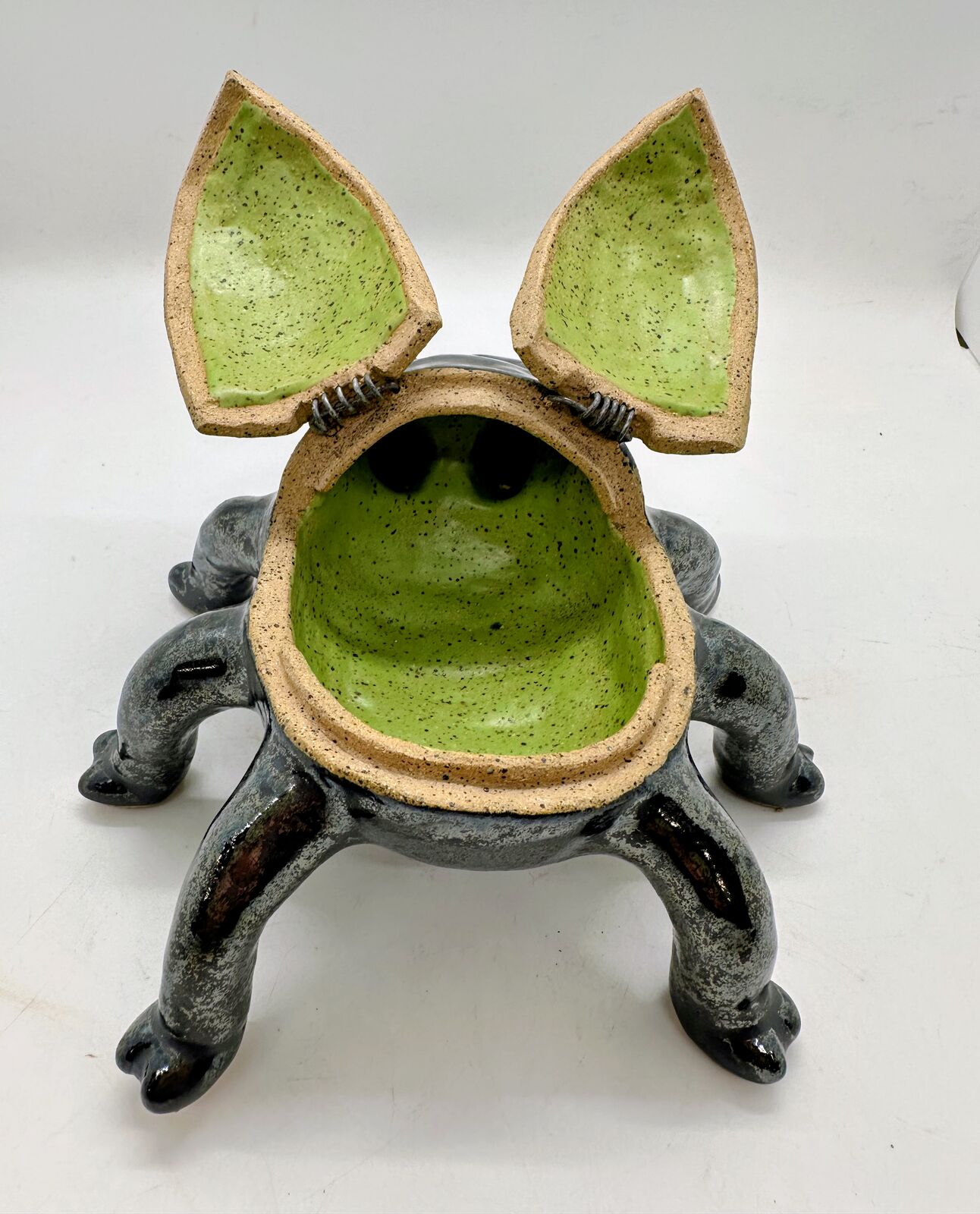 Marshall seen from the front with his wing-case lid flipped open on its wire hinges. The two halves stand up like pointed ears, and the lid and bowl are glazed speckled lime green inside.